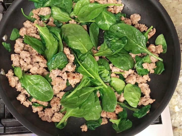 Adding spinach to the cooked sausage.