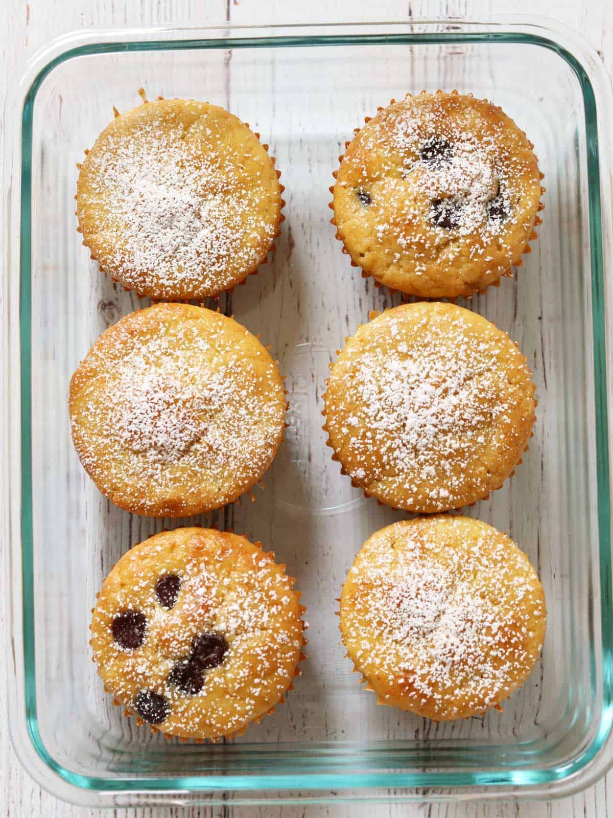 Six almond flour muffins are stored in a glass storage container.