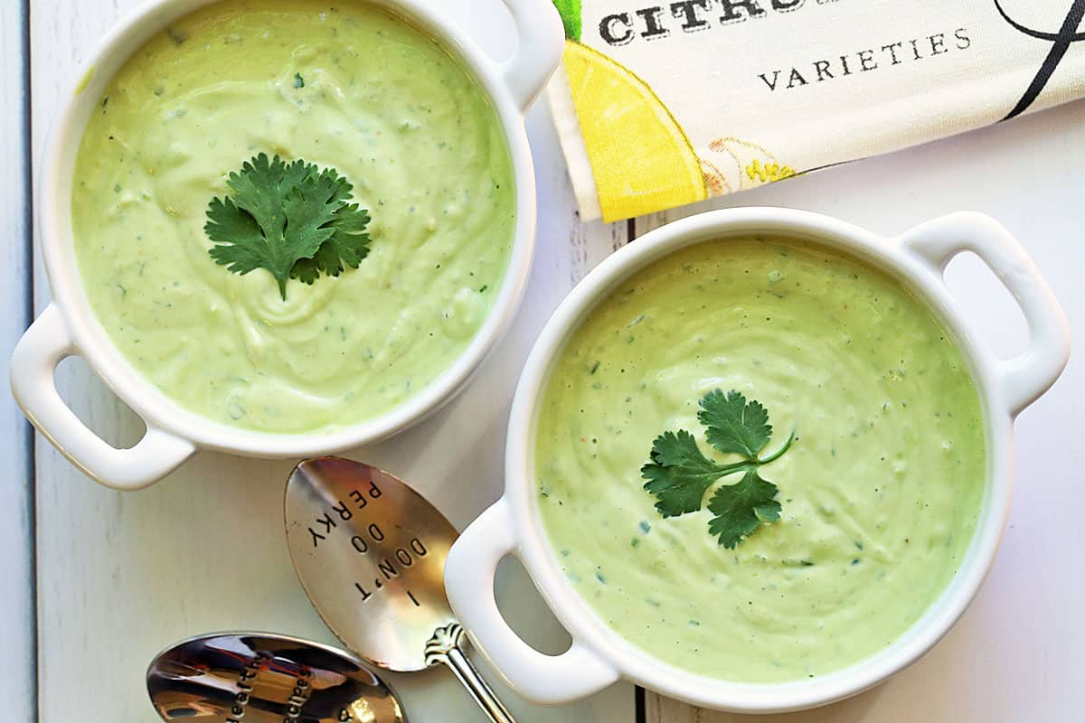 Two bowls of avocado soup are served with spoons.