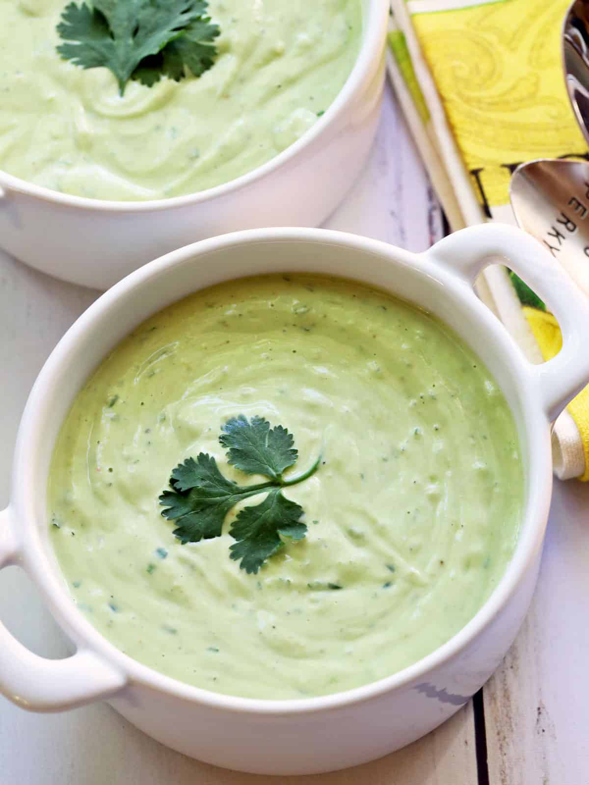 Avocado soup is served in white bowls.