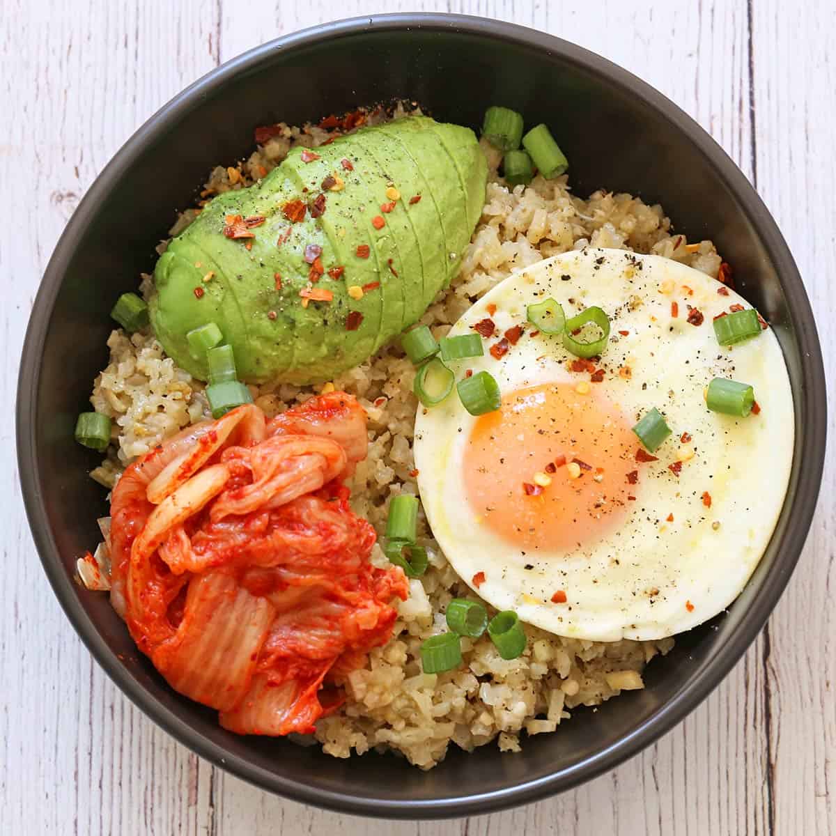 A cauliflower rice bowl with an egg, an avocado, and kimchi.