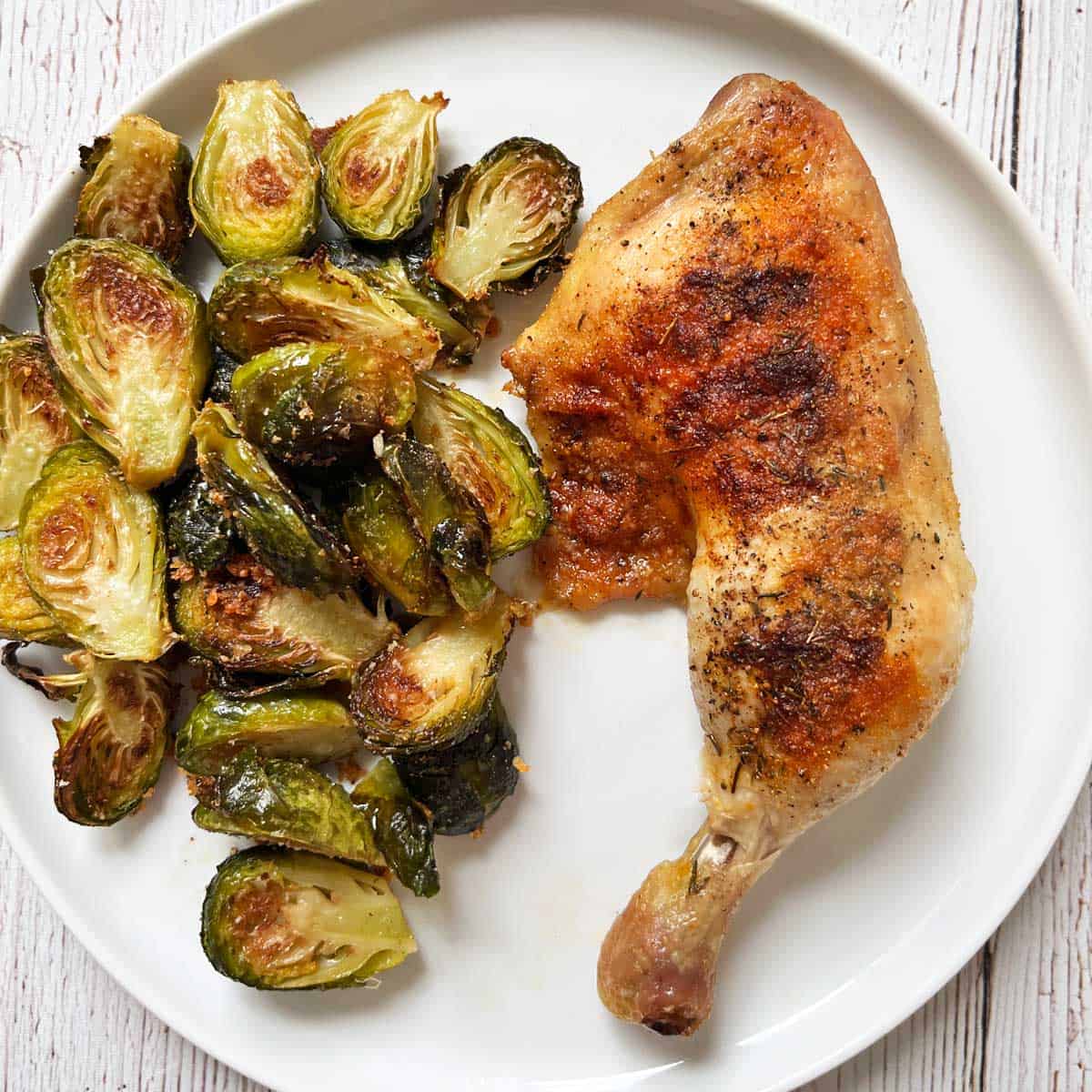 A chicken leg quarter is served with Brussels sprouts.