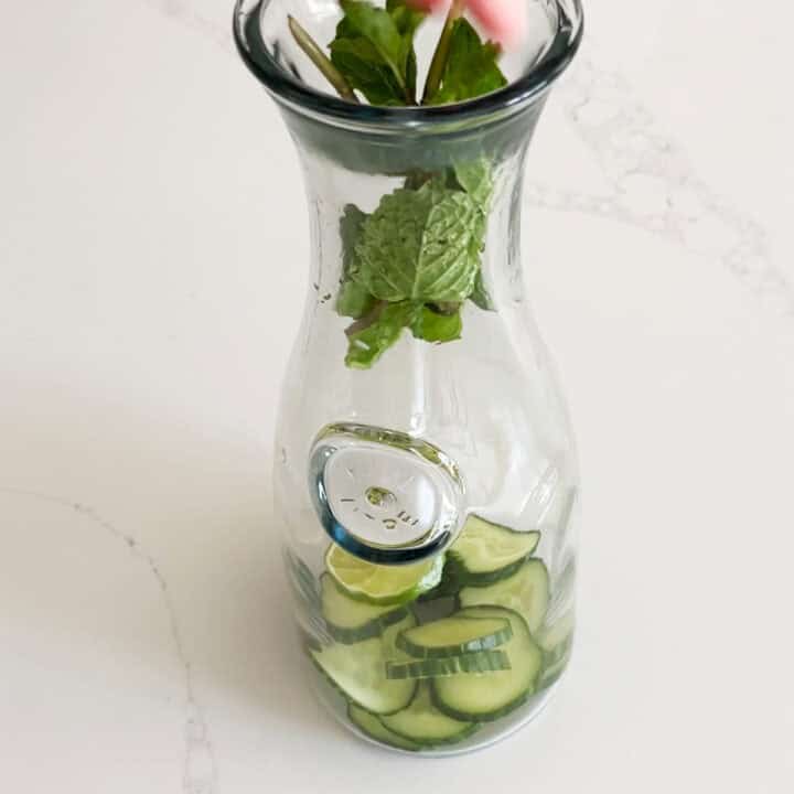 Placing the cucumber, limes, and mint in a pitcher.