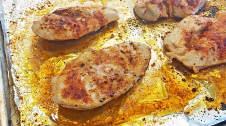 Four cooked chicken breasts on a baking sheet.