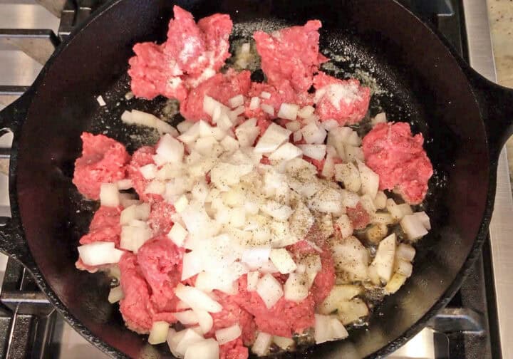 Raw ground beef and chopped onions in a cast-iron skillet.