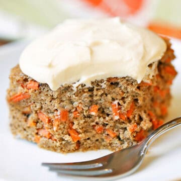 A slice of keto carrot cake is served on a white plate with a fork.