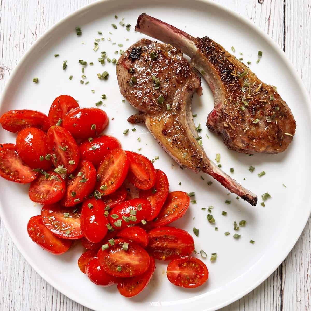 Two lamb chops are served with tomato salad.