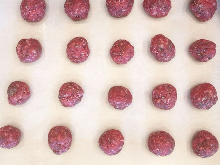 The meatballs are arranged on a parchment-lined baking sheet.