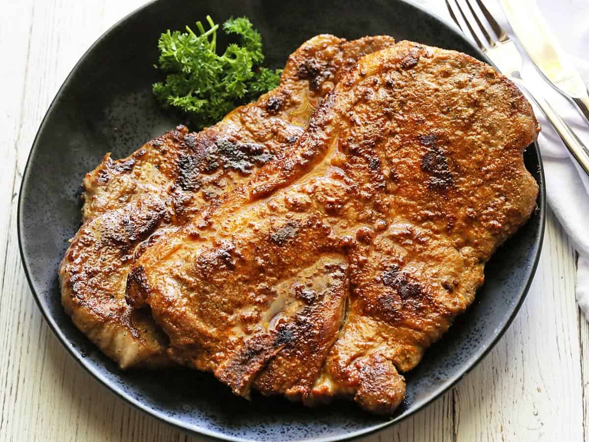 Pork shoulder steaks are served on a plate with silverware.