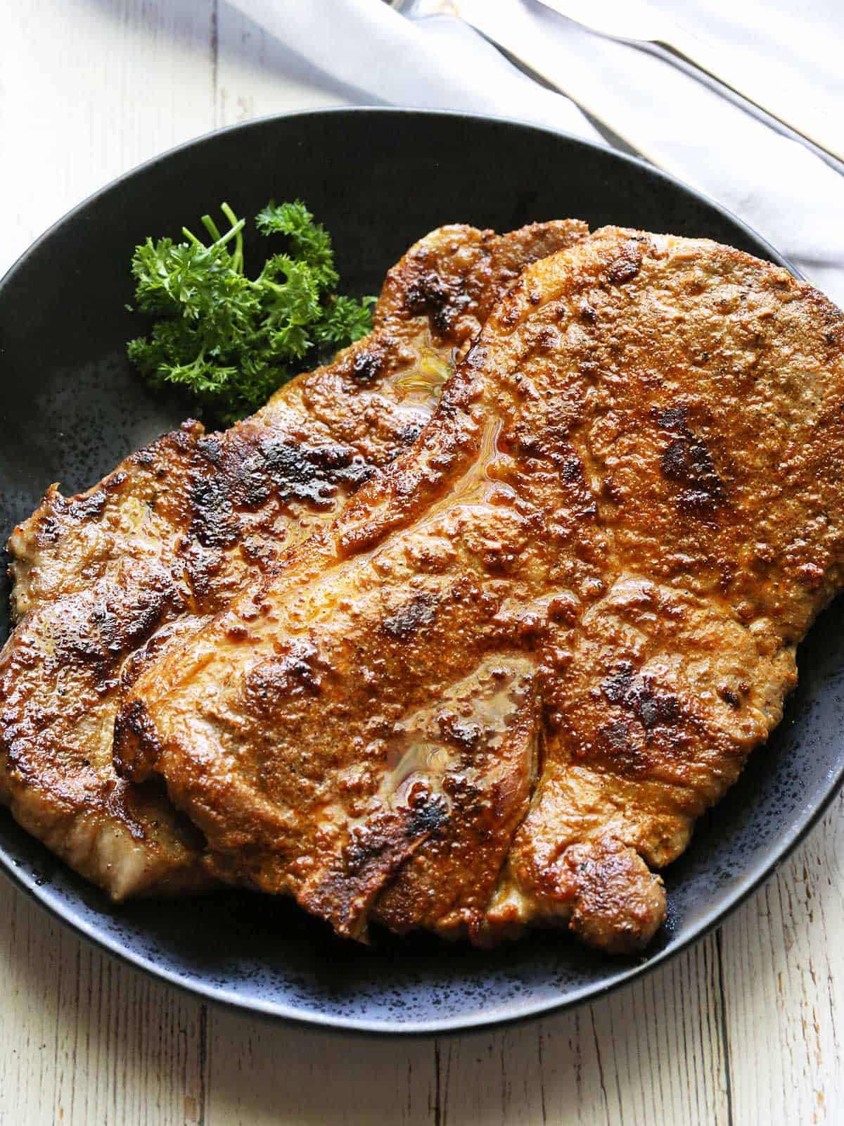 Two pork shoulder steaks are served with a garnish of parsley.