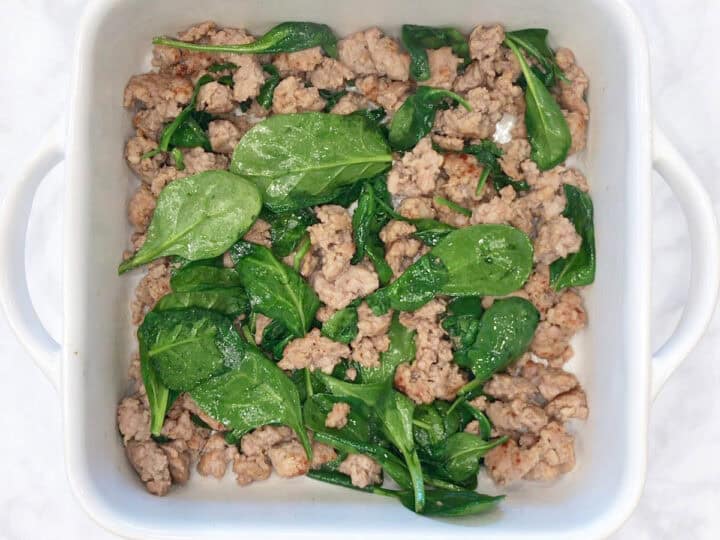Cooked sausage and spinach in a baking dish.