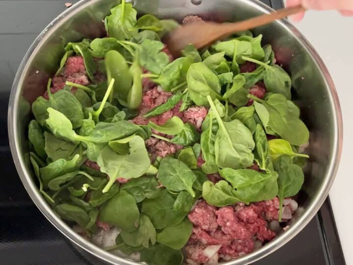 Adding spinach to the meat.