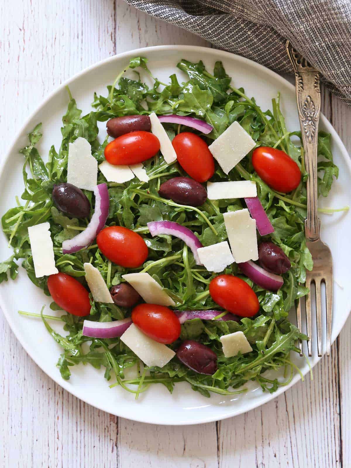Arugula salad is served on a white plate.