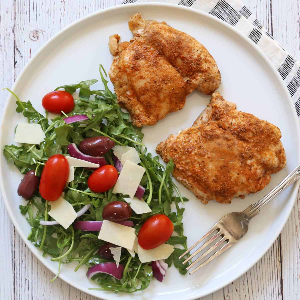 Arugula salad is served as a side dish to boneless chicken thighs.