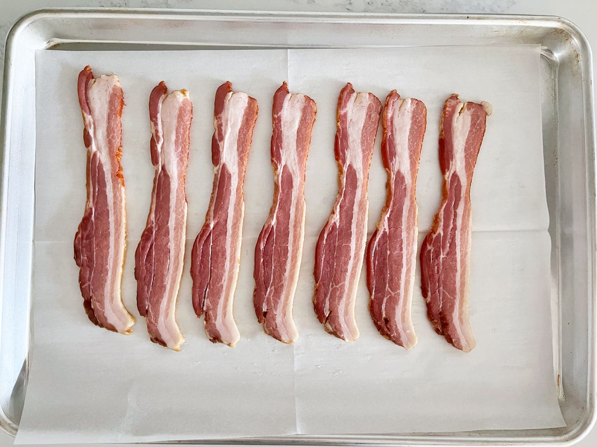 Raw bacon slices on a parchment-lined baking sheet.
