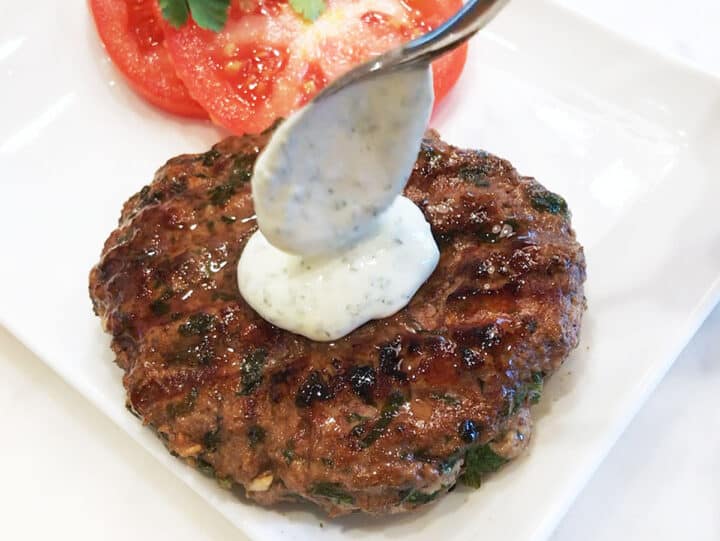 A lamb burger is topped with a dollop of yogurt sauce.