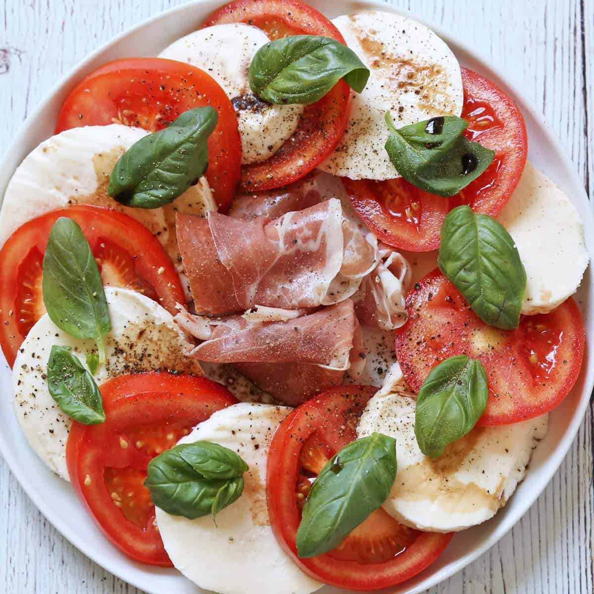 Caprese salad is served with prosciutto.