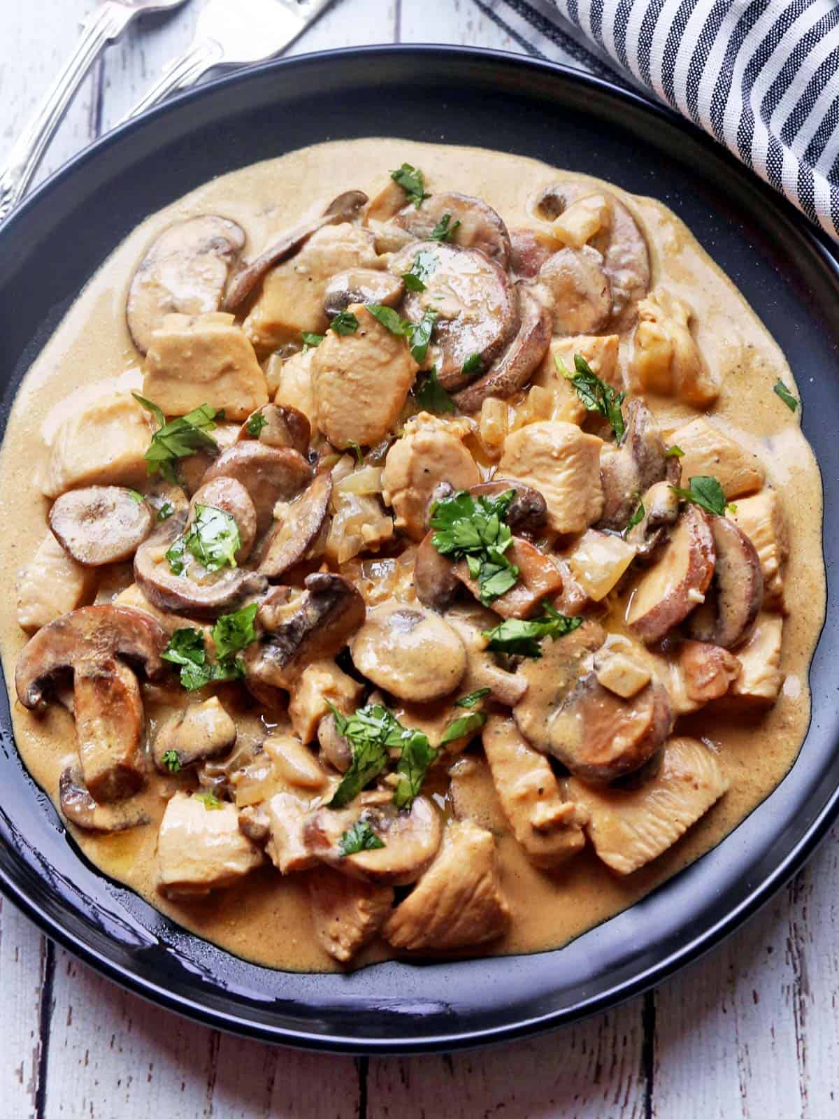 Chicken Stroganoff is served on a black plate with a napkin.