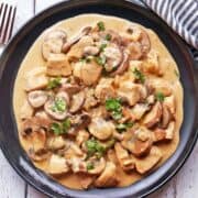 Chicken Stroganoff is served on a black plate with a fork and a napkin.