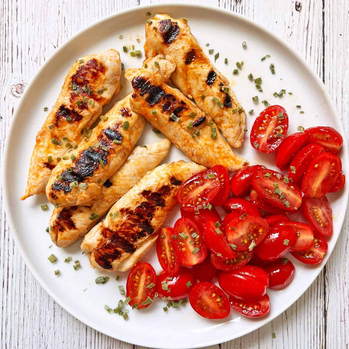 Grilled chicken tenders are served with a tomato salad.