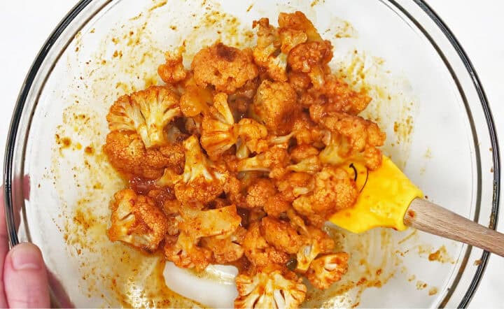 Mixing cauliflower and buffalo sauce in a bowl.