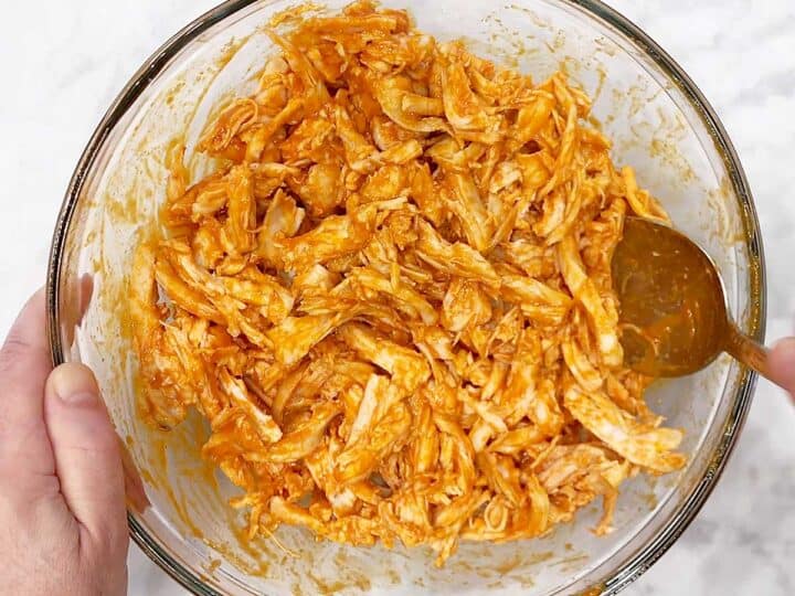 Mixing the shredded chicken and the buffalo sauce in a bowl.