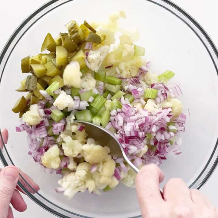Mixing cauliflower, celery, onions, and pickles.