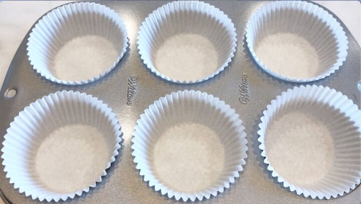 A six-cavity muffin pan is lined with six paper liners.