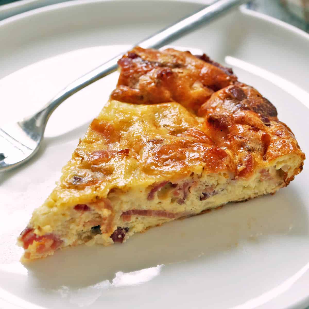 A slice of crustless quiche Lorraine is served on a plate with a fork.
