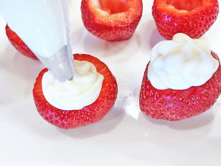 Piping the cream cheese into the strawberries.