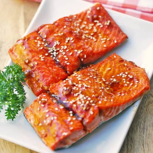 Two teriyaki salmon fillets are served on a white plate.