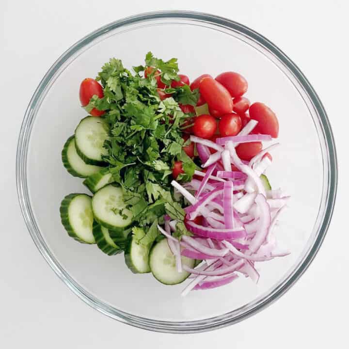 Tomatoes, cucumbers, red onions, and cilantro in a salad bowl.