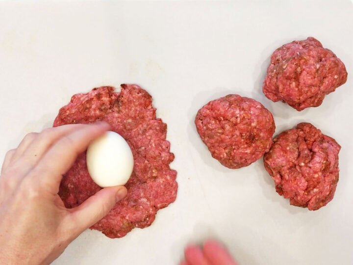 Wrapping an egg in ground beef.