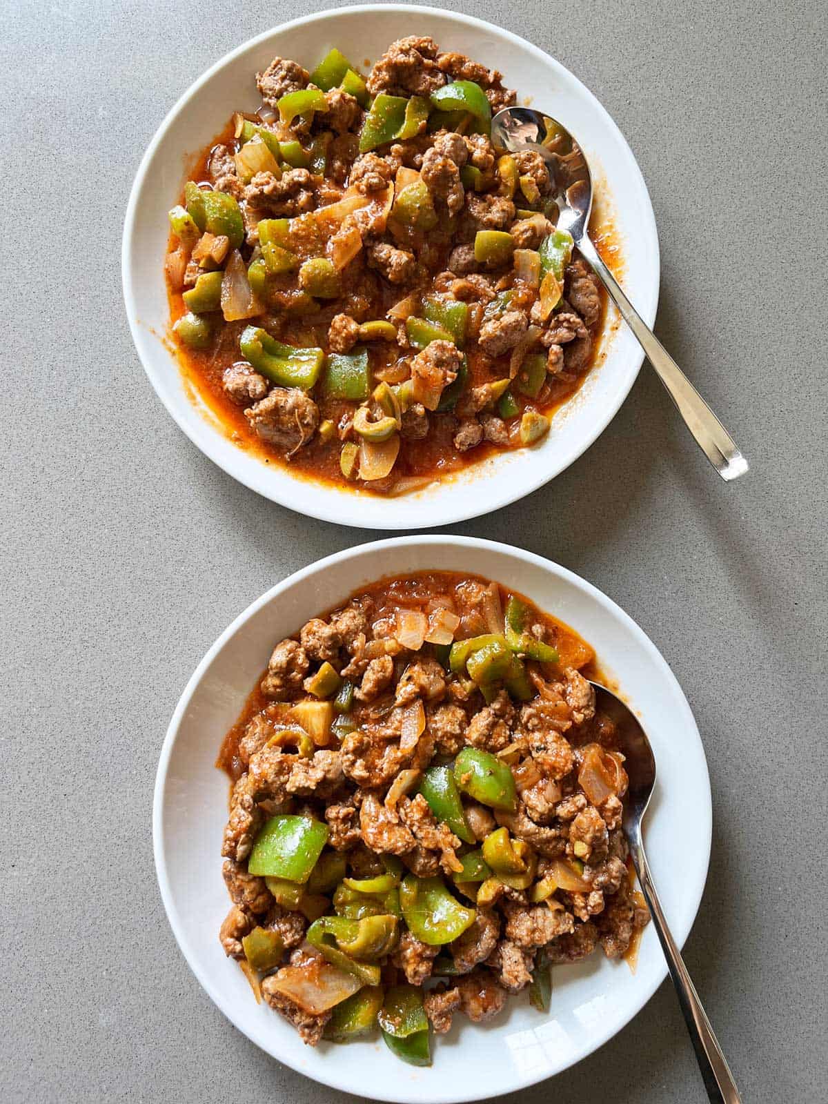 Two plates of Picadillo, served with spoons.