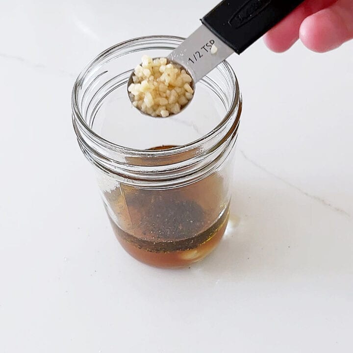 Adding minced garlic to the jar with the salad dressing.