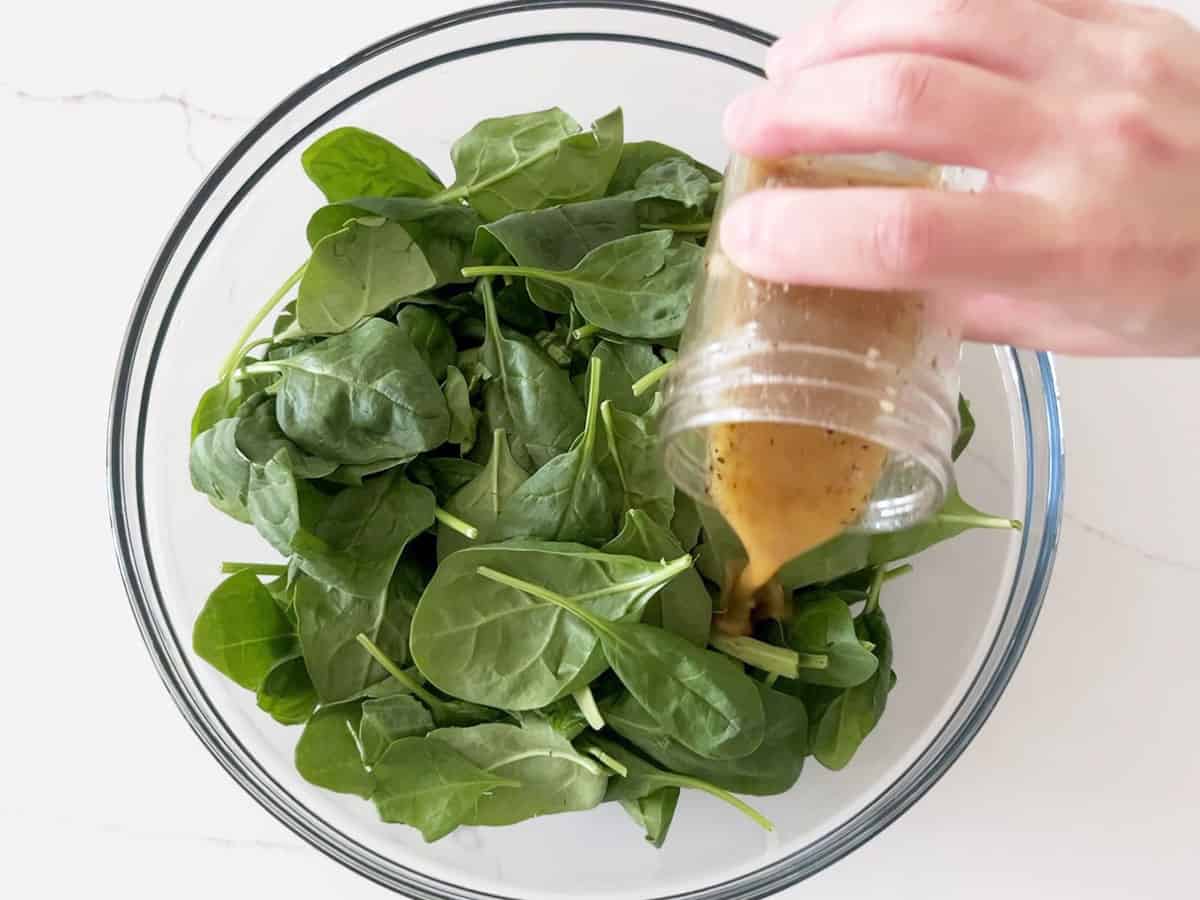 Pouring the dressing on the spinach leaves.