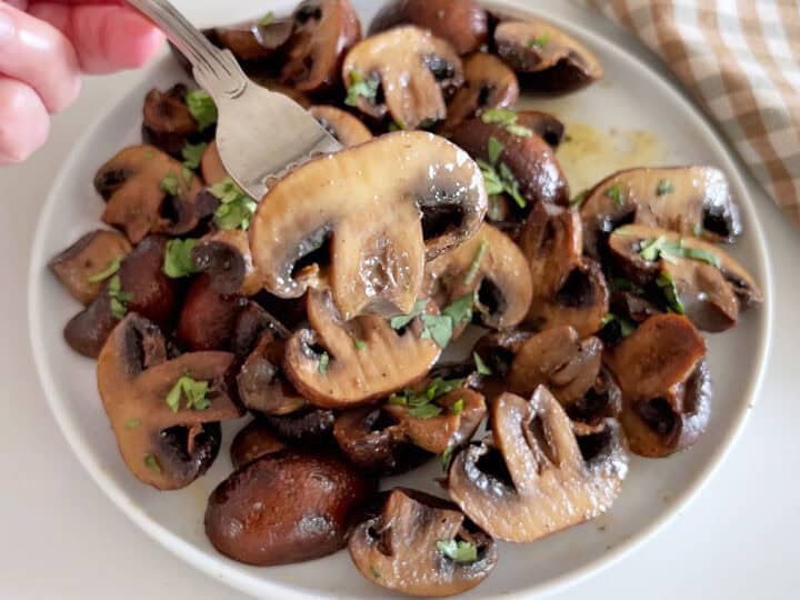 The mushrooms are served. A fork lifts one of them off the plate.