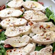 Poached chicken slices are served on top of spinach salad.