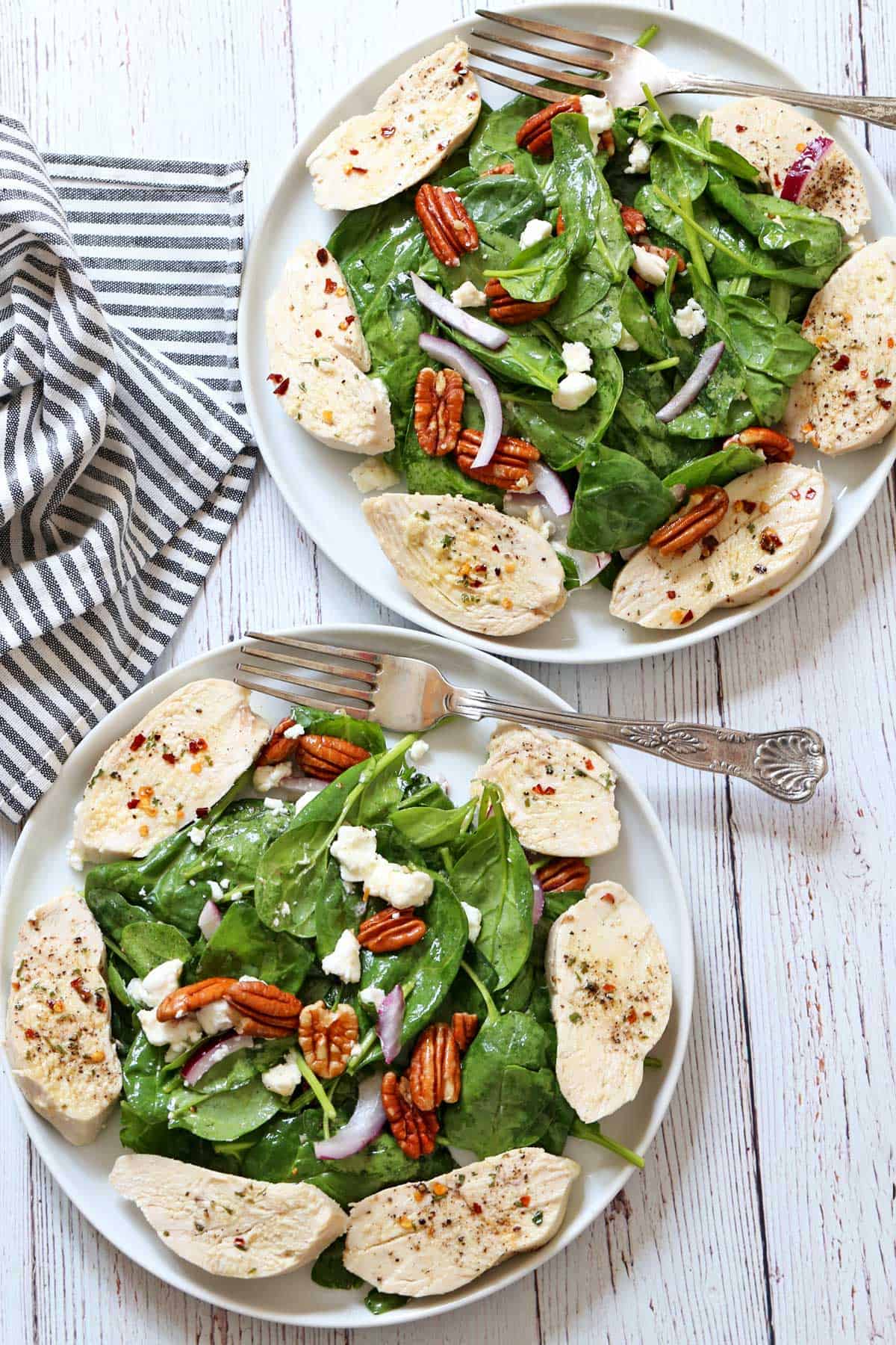 Two plates with spinach salad and poached chicken.