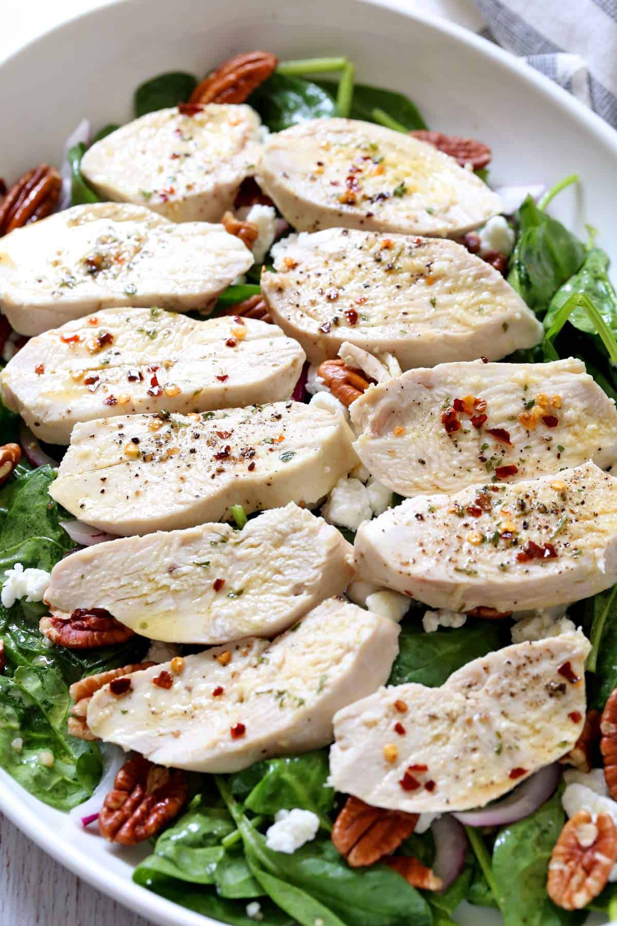 Poached chicken slices are served on top of spinach salad.