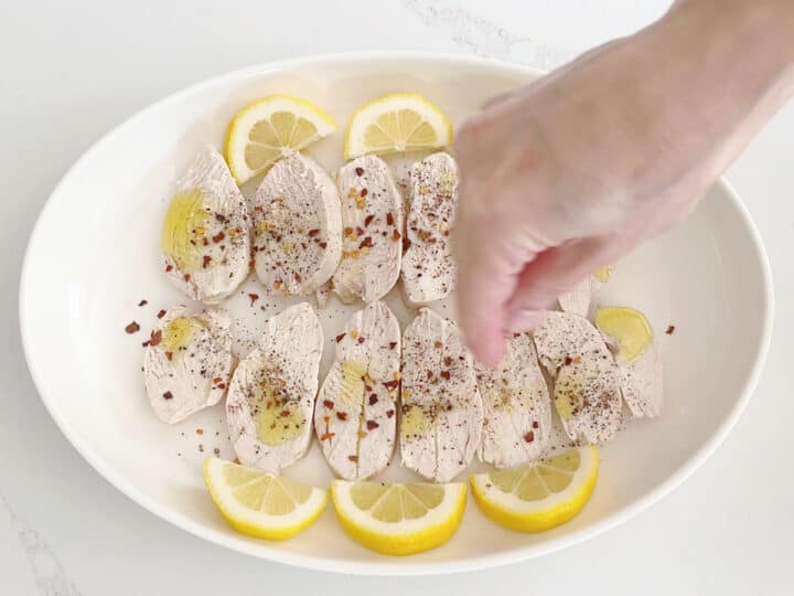 Seasoning the chicken with red pepper flakes.