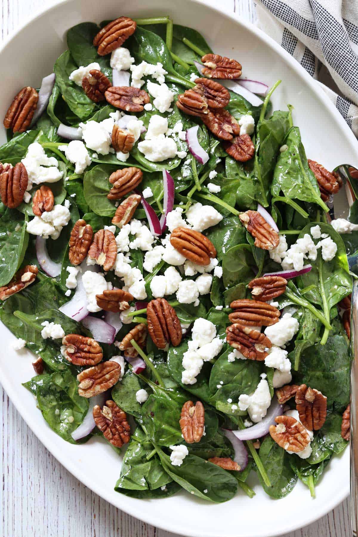 Spinach salad is served on a white platter.