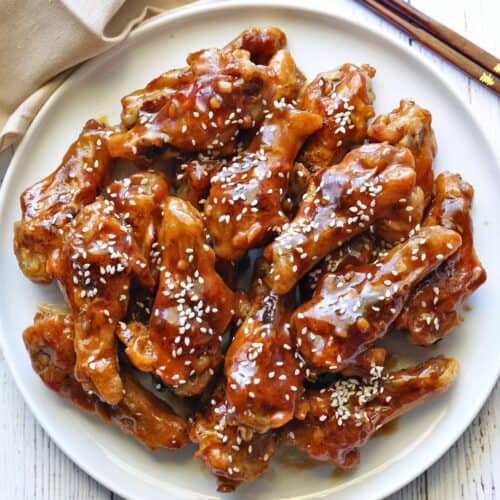 Teriyaki chicken wings are served on a white plate with chopsticks.