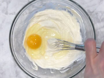 Adding an egg to the cheesecake mixture.