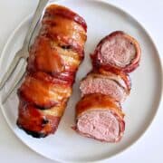 Bacon-wrapped pore tenderloin is served on a white plate.