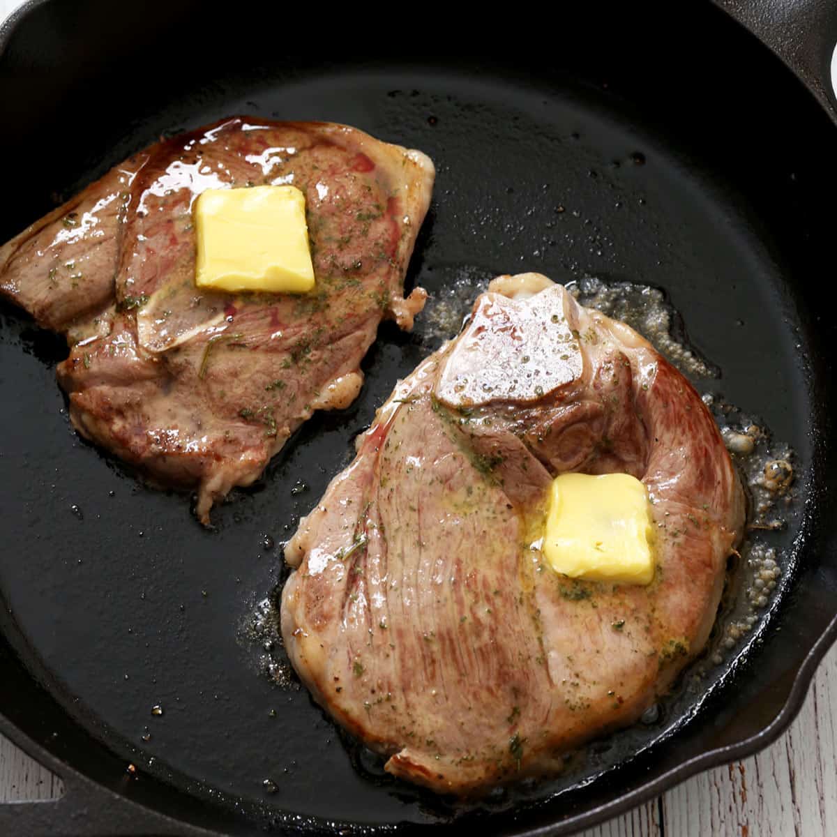 Two lamb steaks are topped with butter.