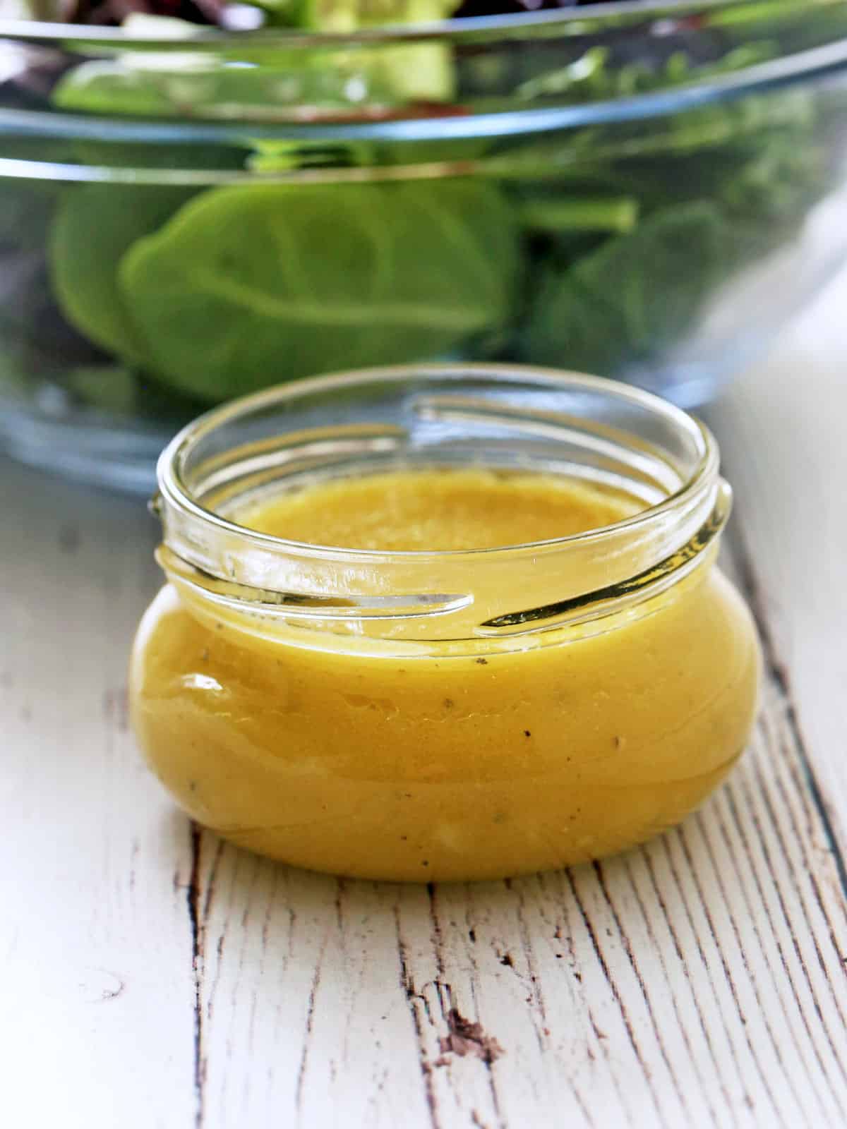 Vinaigrette is served in a jar next to a bowl with mixed salad greens.