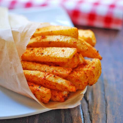 Jicama fries are served on a white plate wrapped in parchment paper.
