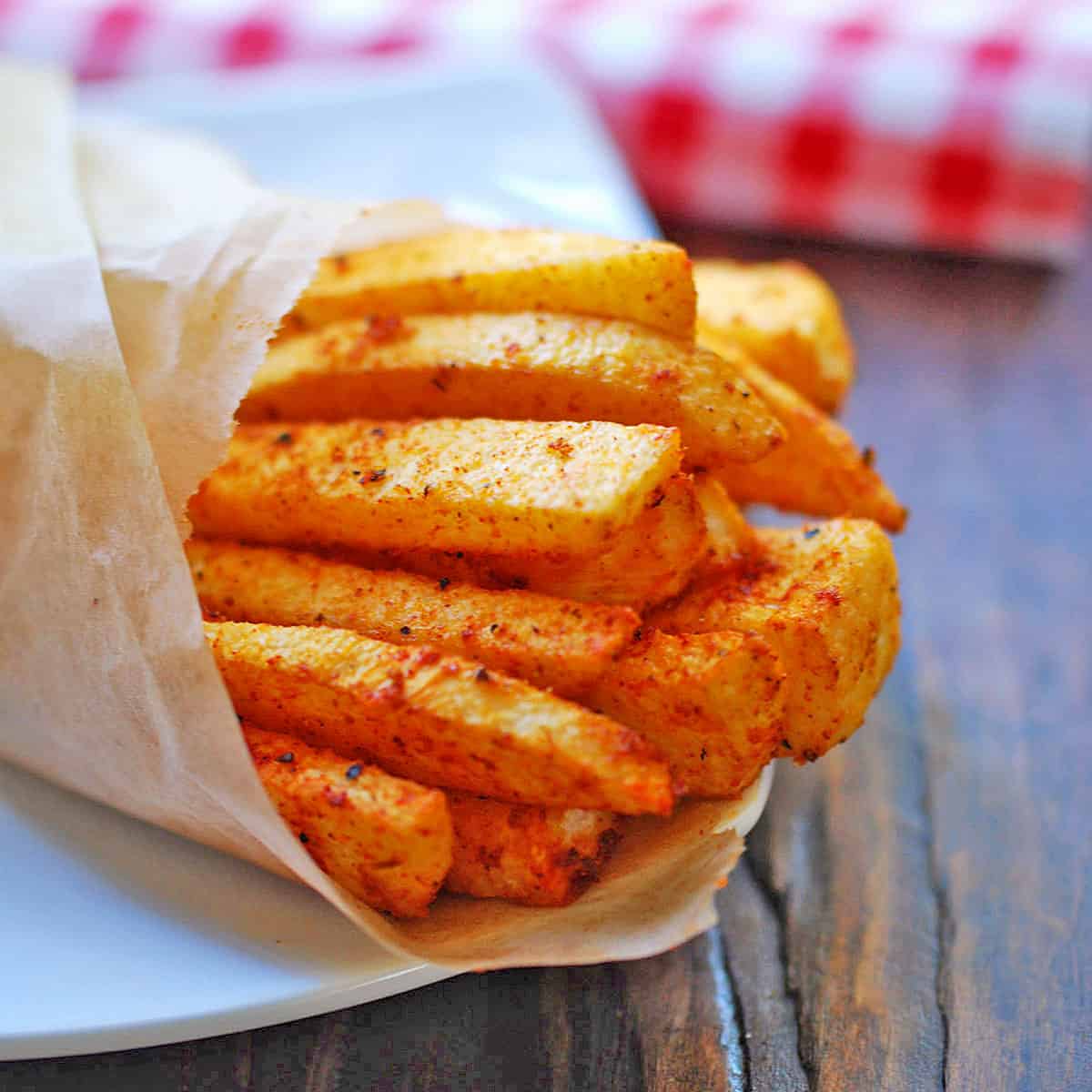 Jicama fries are served on a white plate wrapped in parchment paper.