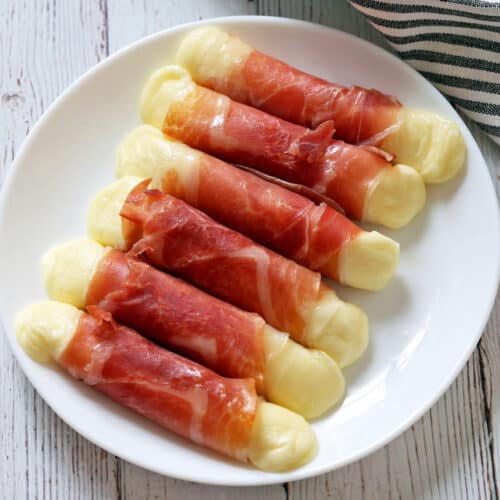 Prosciutto wrapped mozzarella is served on a white plate.